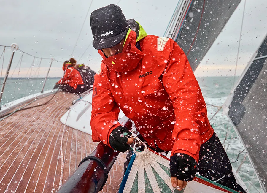 Sailor in a red foul-weather jacket on a yacht deck in spray