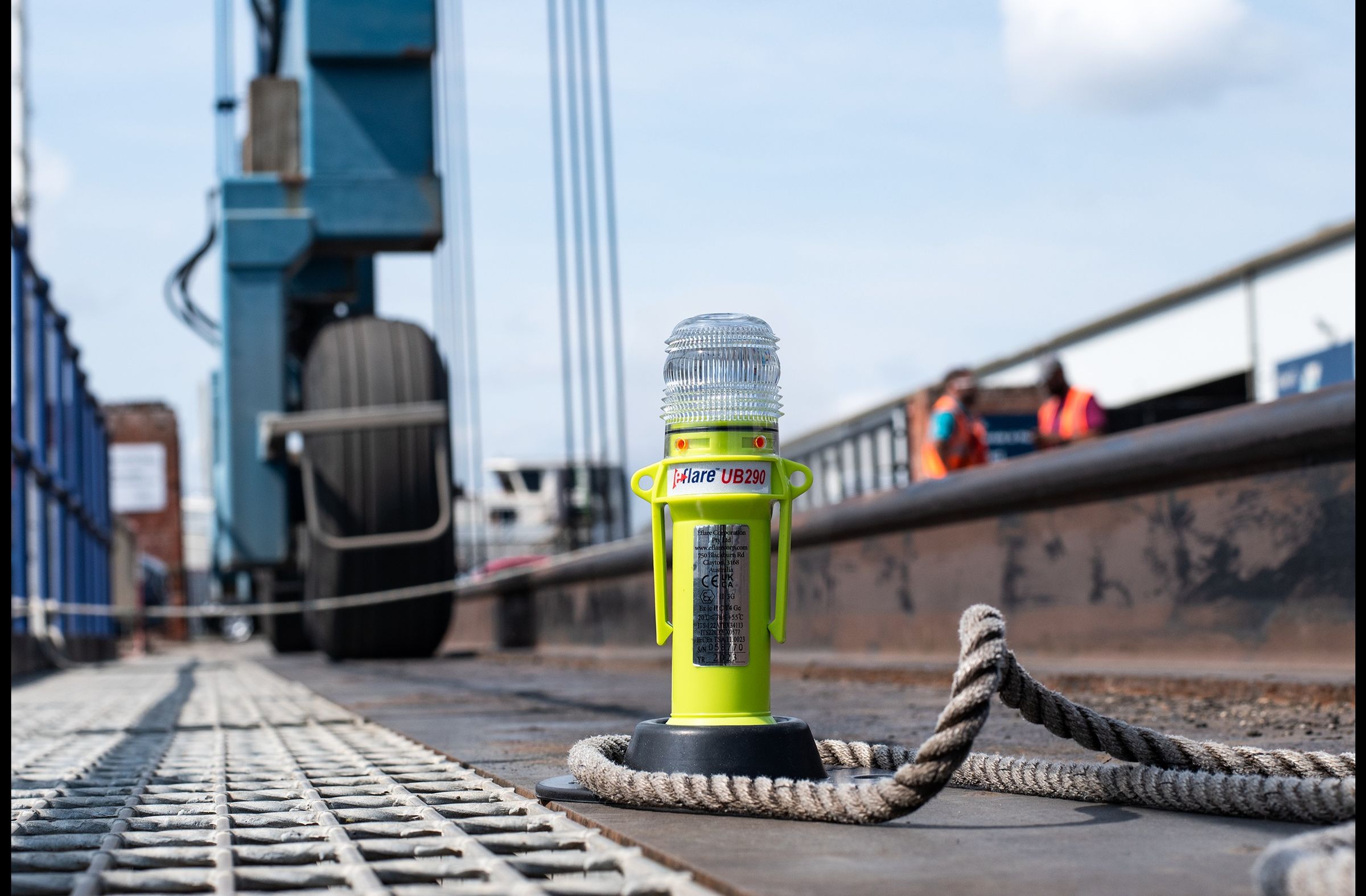 Yellow LED safety light on a metal deck beside coiled rope, with a port crane behind