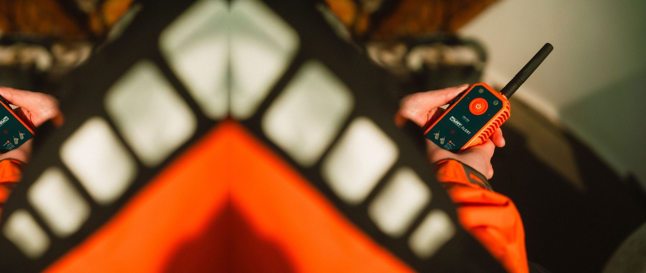 Hand holding a compact man overboard beacon against an orange lifejacket