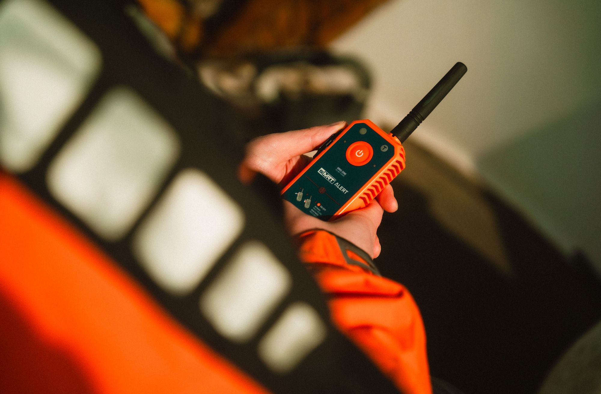 Hand holding a compact sMRT man overboard beacon against an orange lifejacket